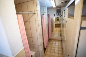 A public restroom with beige stalls, tiled walls, pink shower curtains, and a row of sinks and mirrors at the far end.